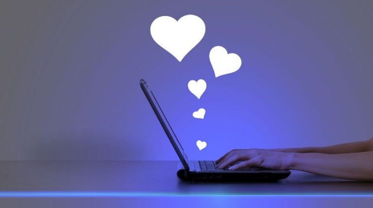 Hands on a laptop, with white heart icons coming up out of the screen.