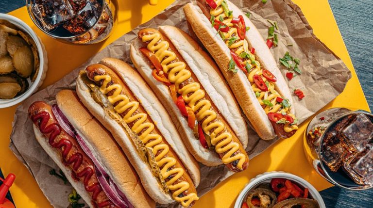 A plate with four hot dogs covered in different toppings.