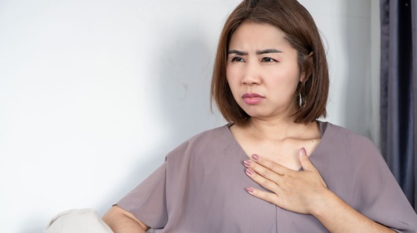 A woman holding a hand to her chest, experiencing heartburn.