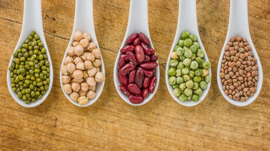 Five white spoons holding different grains and beans.